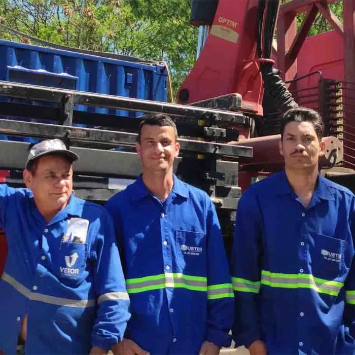 Três colaboradores da Vetor de uniforme azul diante de containers