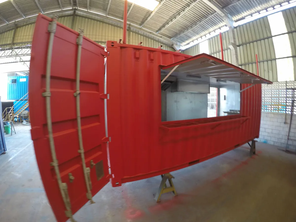 Container vermelho sendo adaptado em lanchonete, com a janela de atendimento aberta, dentro do galpão