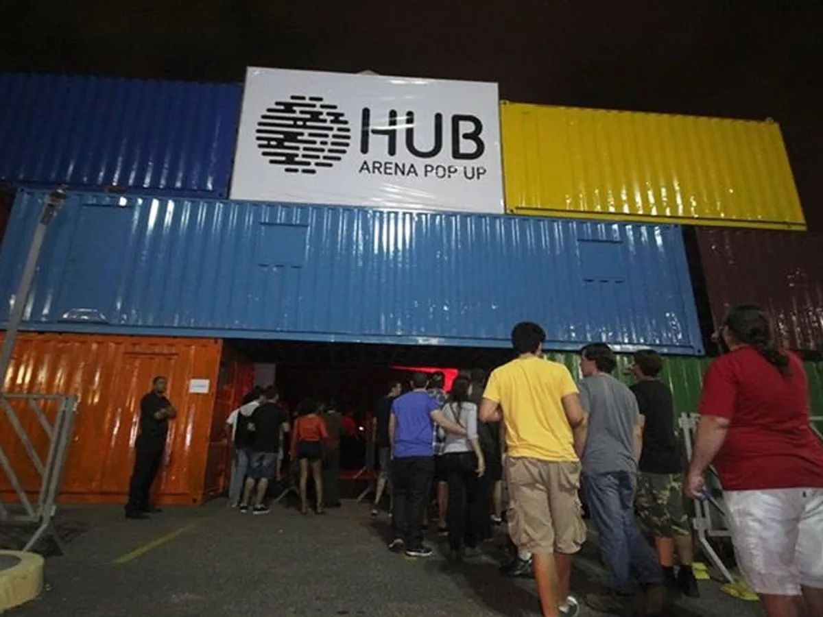 Fachada de containers coloridos empilhados na entrada do centro de eventos, com público na fila